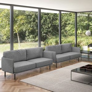 Dos sofás grises de tela con estructura metálica en una sala con grandes ventanales.
